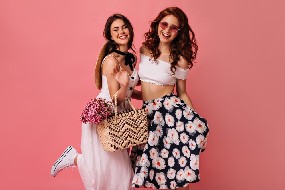 Two women in summer fashion on a pink background